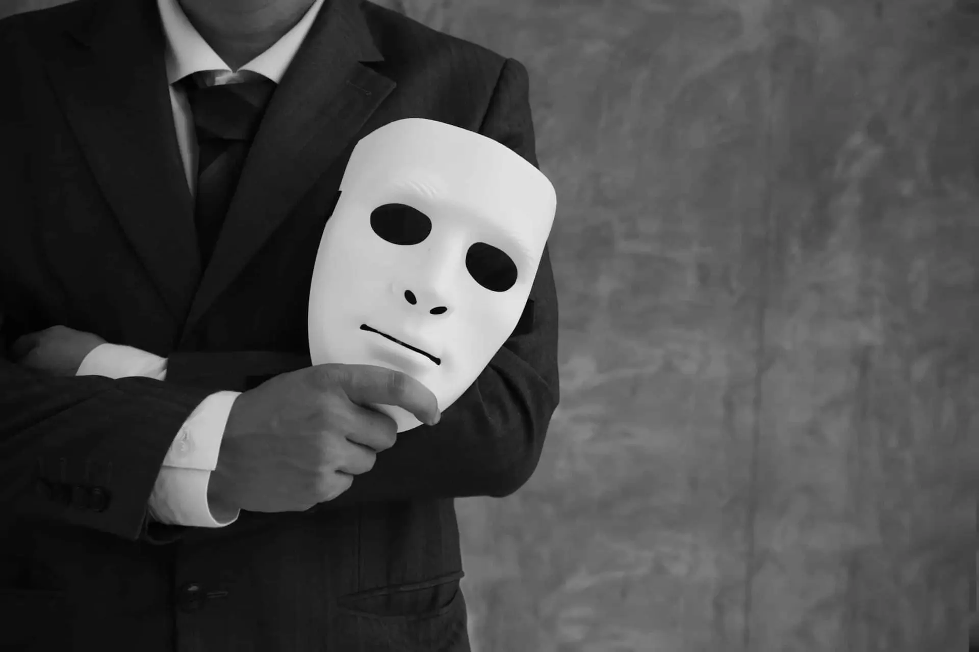 Person hält eine weiße Maske vor dem Körper als Symbol für Offenheit, Vertrauen und das Sichtbarmachen unausgesprochener Themen im Unternehmen.
